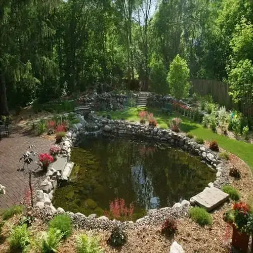 Large backyard pond with stream, stone bridge, and surrounding gardens
